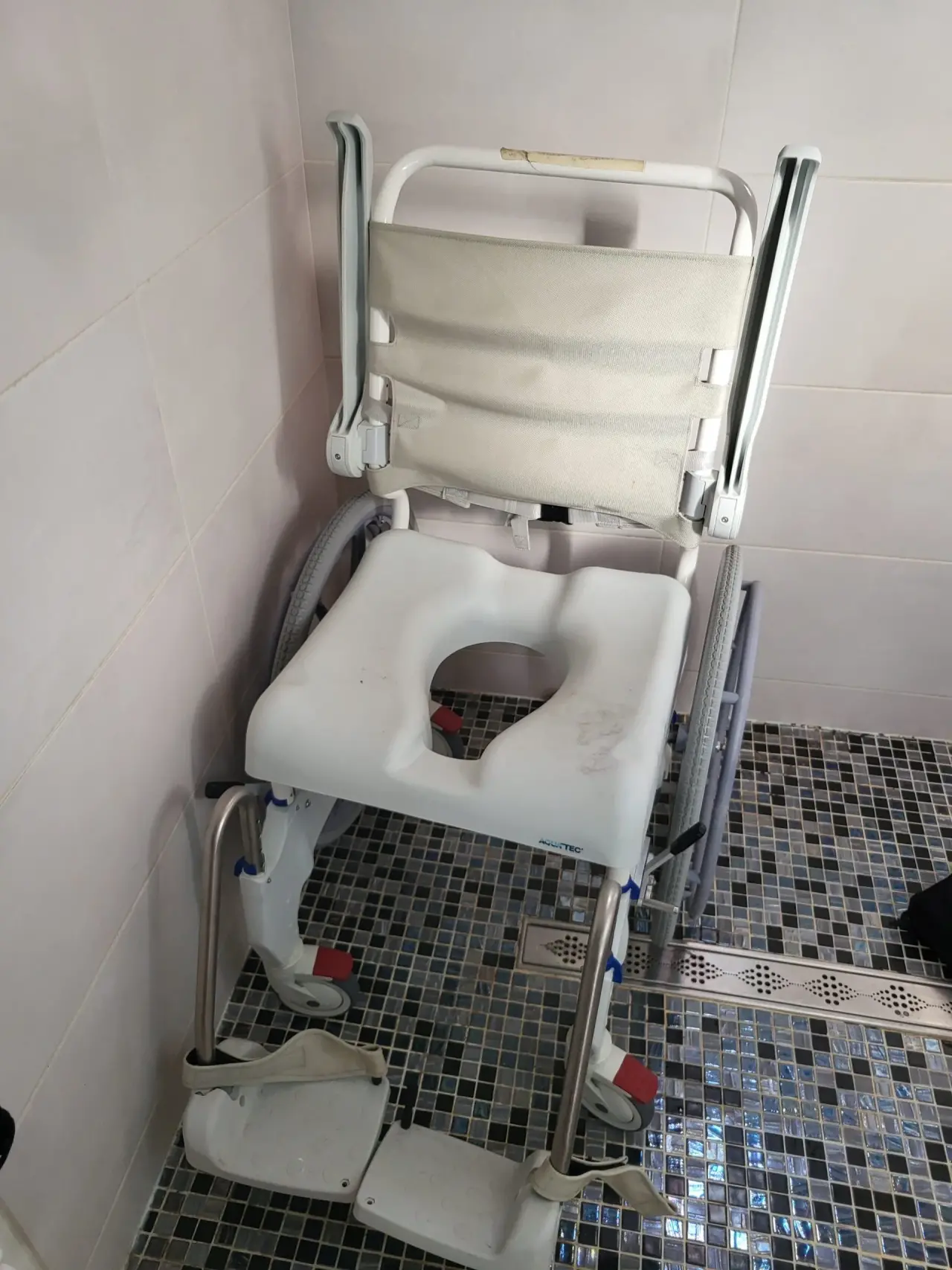 Fauteuil roulant de douche et toilettes AQUATEC, blanc et gris clair, en métal, plastique et textile, usagé, avec assise percée