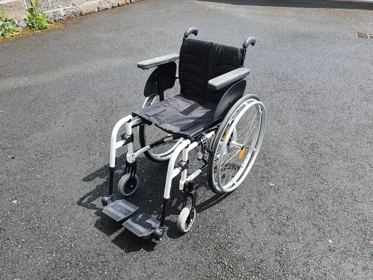 Fauteuil roulant manuel blanc et noir en métal et textile, en bon état général, avec des repose-