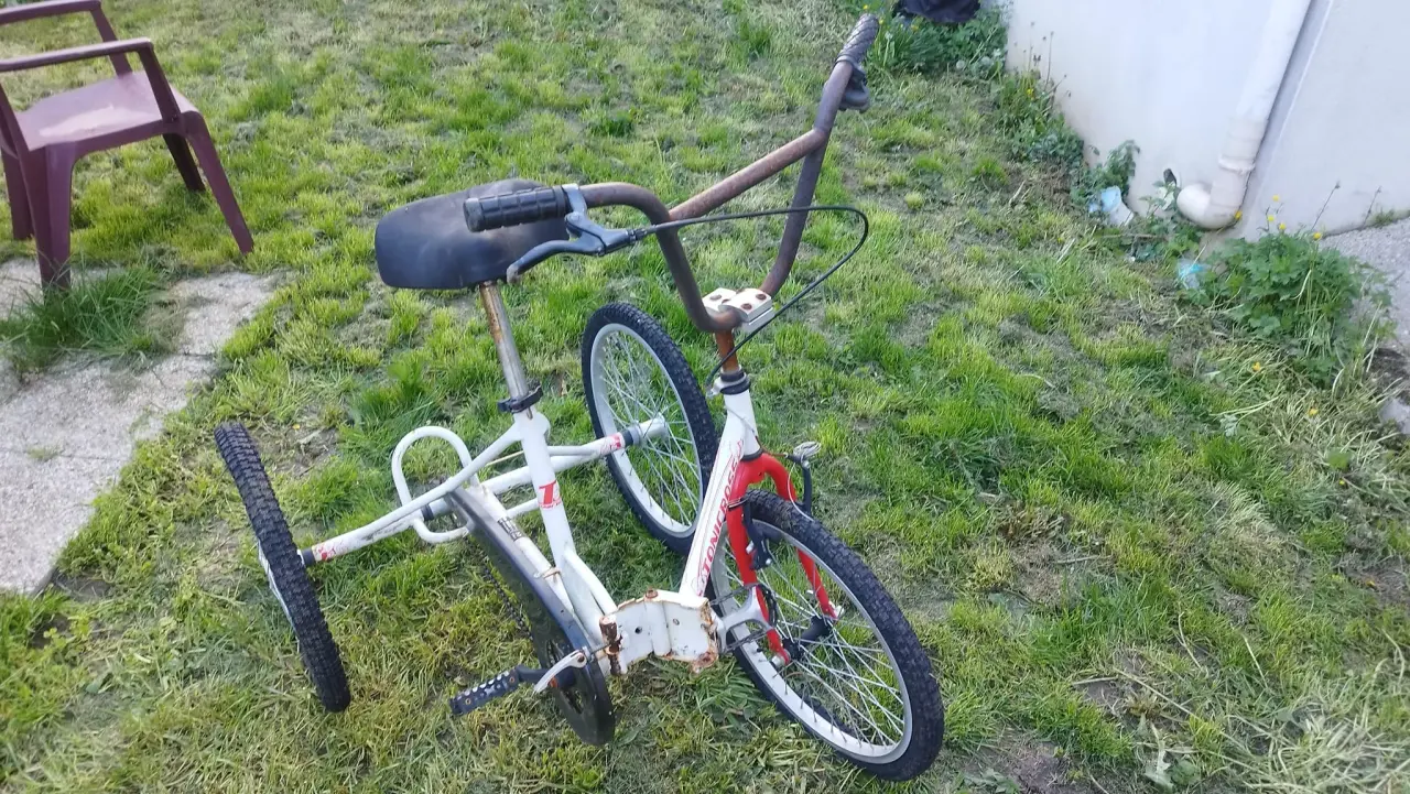 Tricycle couché blanc et rouge en métal, usagé et rouillé, doté d'un cadre allongé