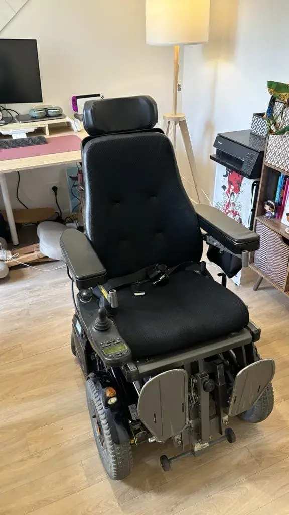 Fauteuil roulant électrique noir, structure en métal et assise en tissu, en bon état général, doté d'un joystick de commande intuitif et de repose-pieds ajustables