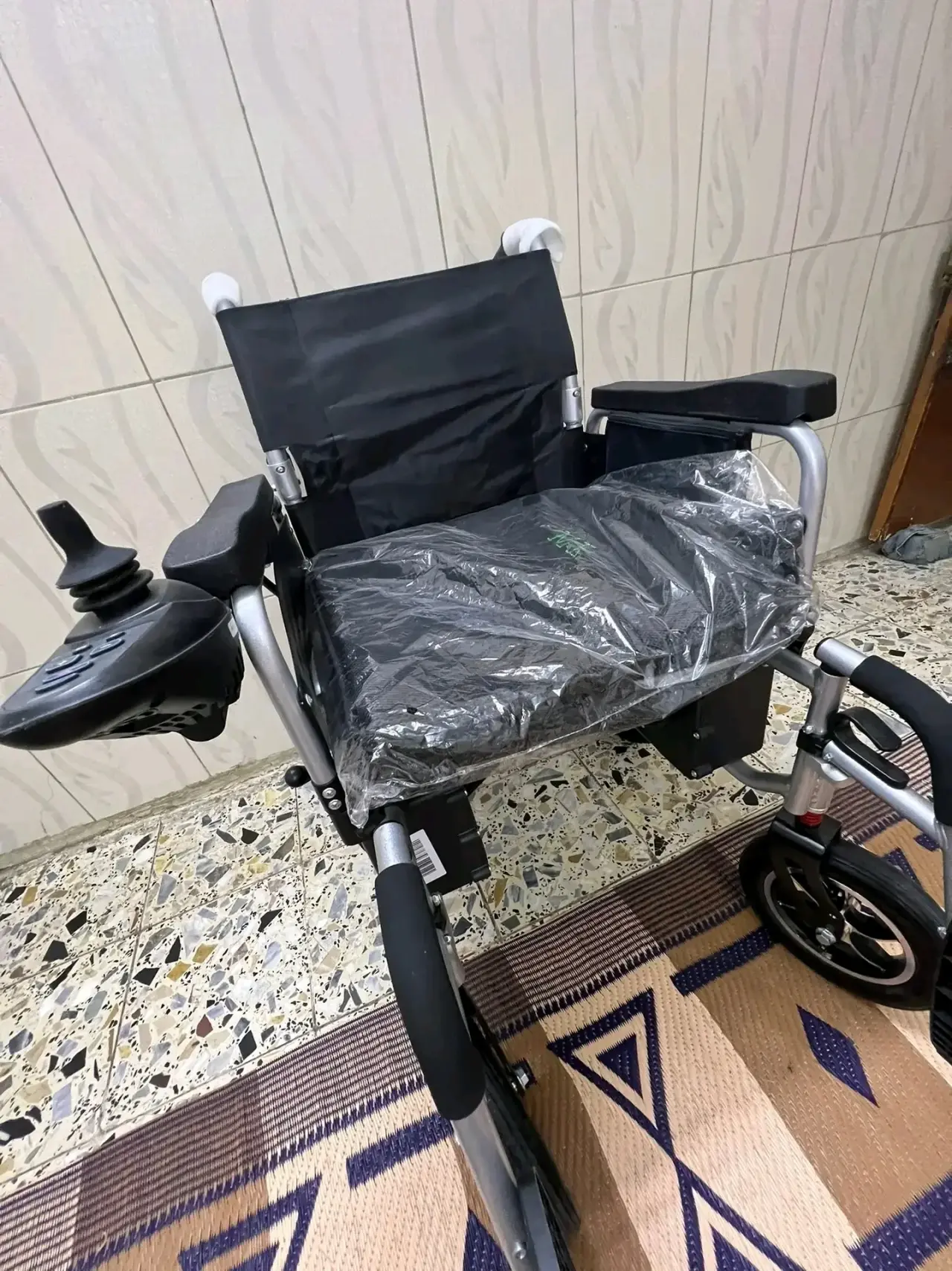 Fauteuil roulant électrique noir et argenté en tissu et aluminium, neuf sous emballage plastique, avec joystick