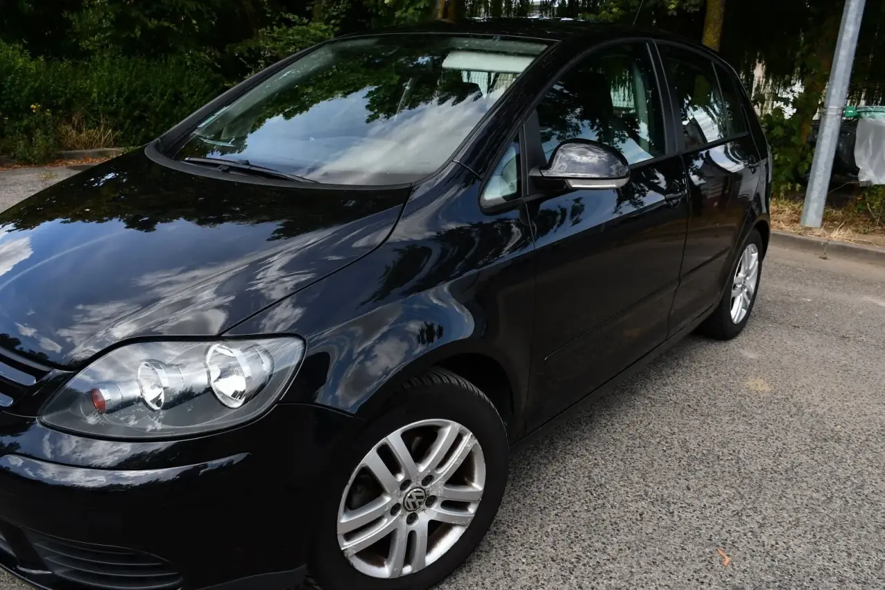 Monospace compact noir brillant, doté de jantes alliage. Sa carrosserie et son verre propres reflètent distinctement le ciel nuageux