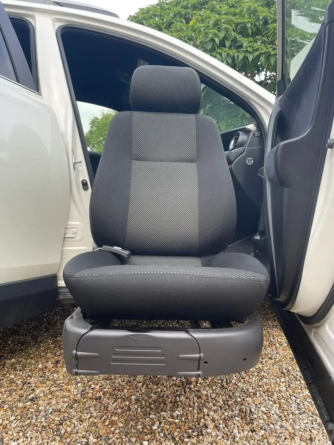 Siège de voiture pivotant d'assistance, en tissu bicolore gris foncé et gris clair à motif, monté sur une base motorisée en plastique