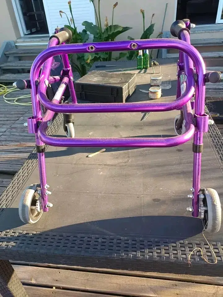 Déambulateur à roulettes pliable en métal violet, avec poignées noires, en bon état général malgré quelques traces