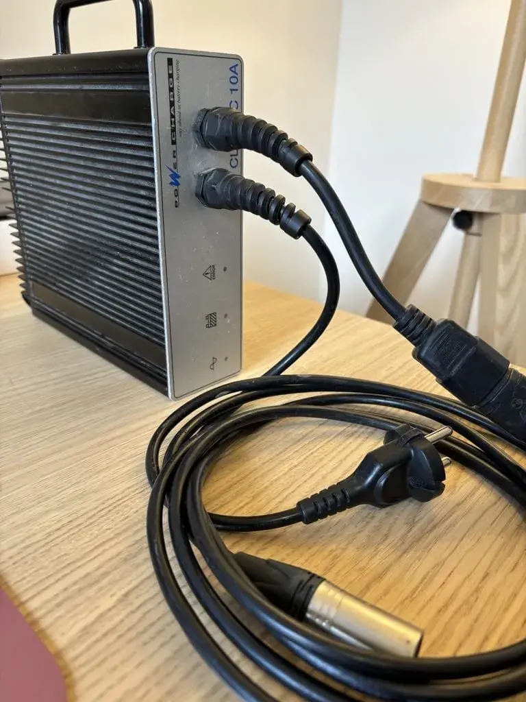 Chargeur de batterie robuste noir à boîtier métallique nervuré et façade grise, en bon état général, avec poignée
